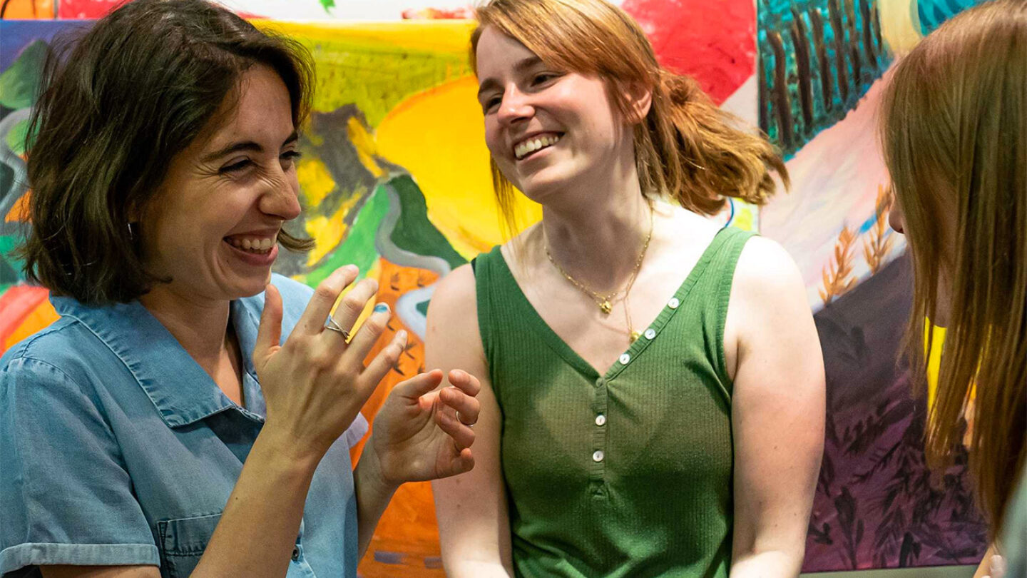 Three young women smiling in front of an abstract and colourful painting.